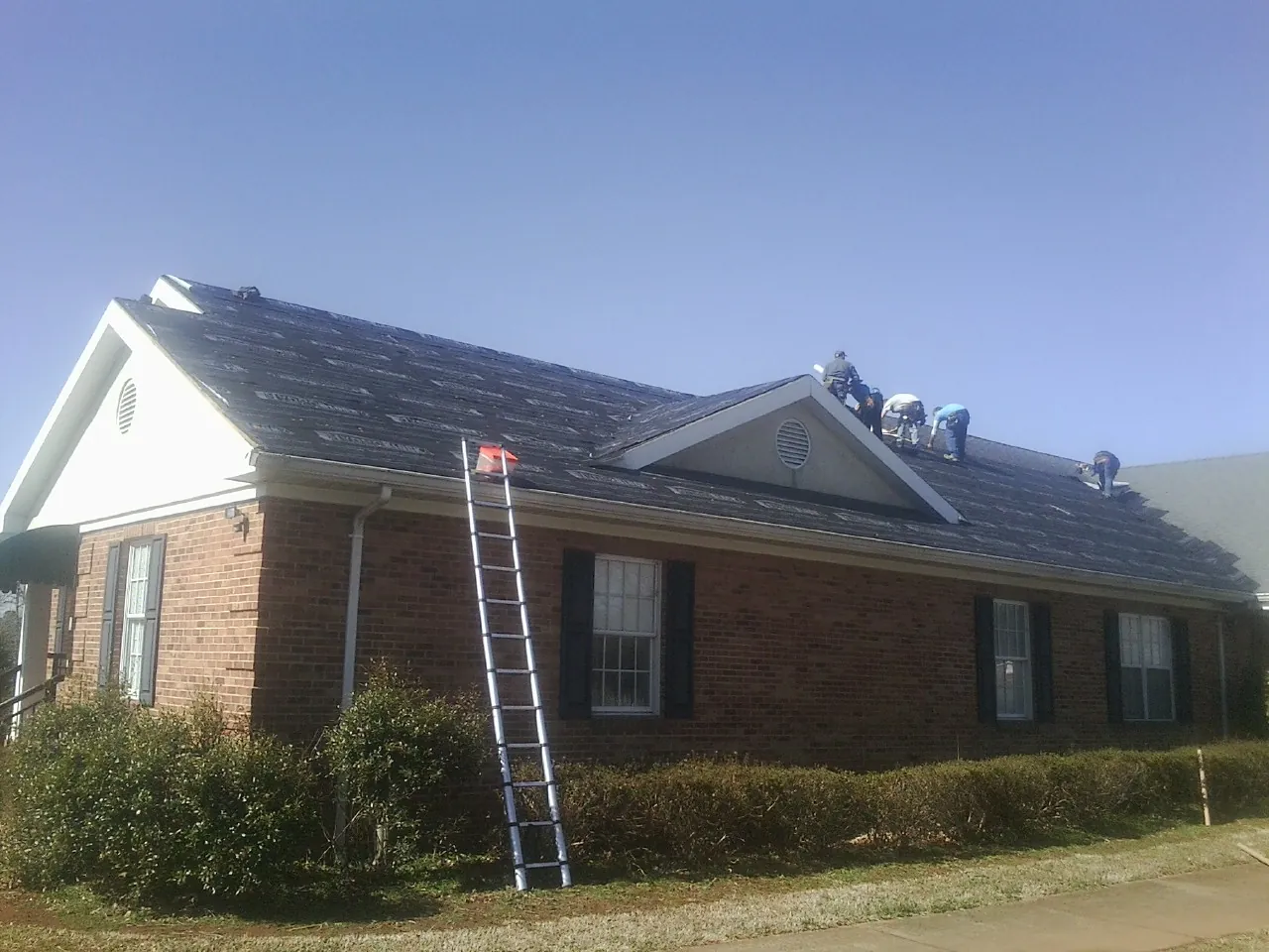 Crew tearing shingles off a brick ranch roof with a ladder set — Metal Roof Repair work by our crew in Gold Hill