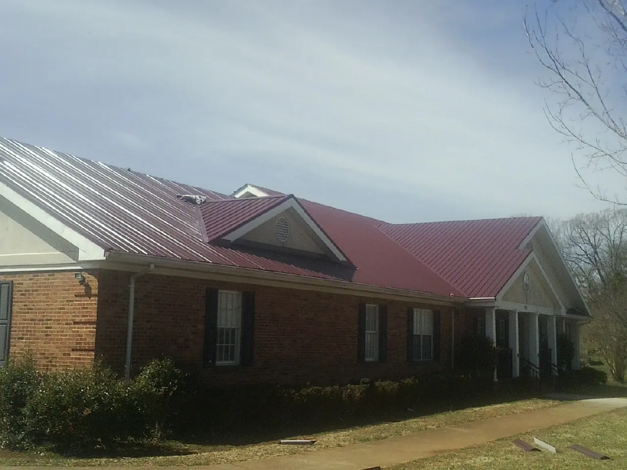 Red metal roof with gabled entries on a long brick building, from a Hail Damage Roof Repair job in Gold Hill