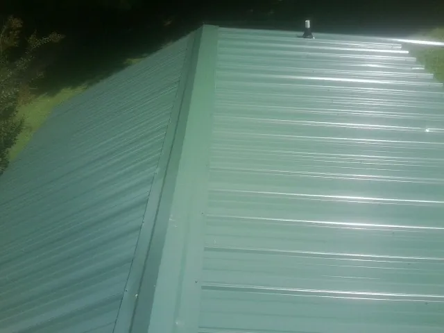 New green metal panels meeting at the ridge of a roof — Flat Roof Repair work by our crew in Gold Hill