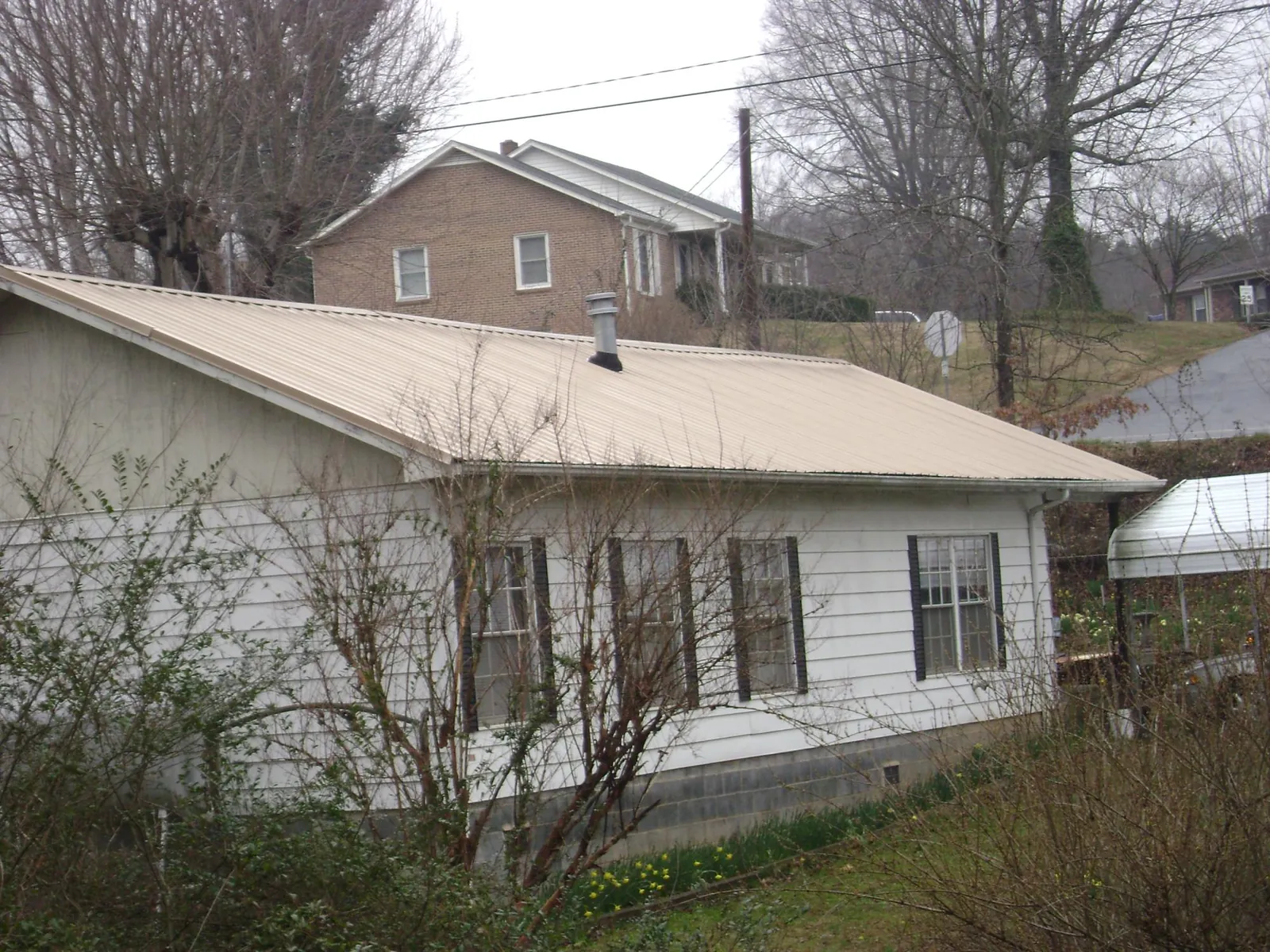 Tan metal roof on a white sided house set into a hillside — Commercial Roofing by Roofing Brothers in Gold Hill